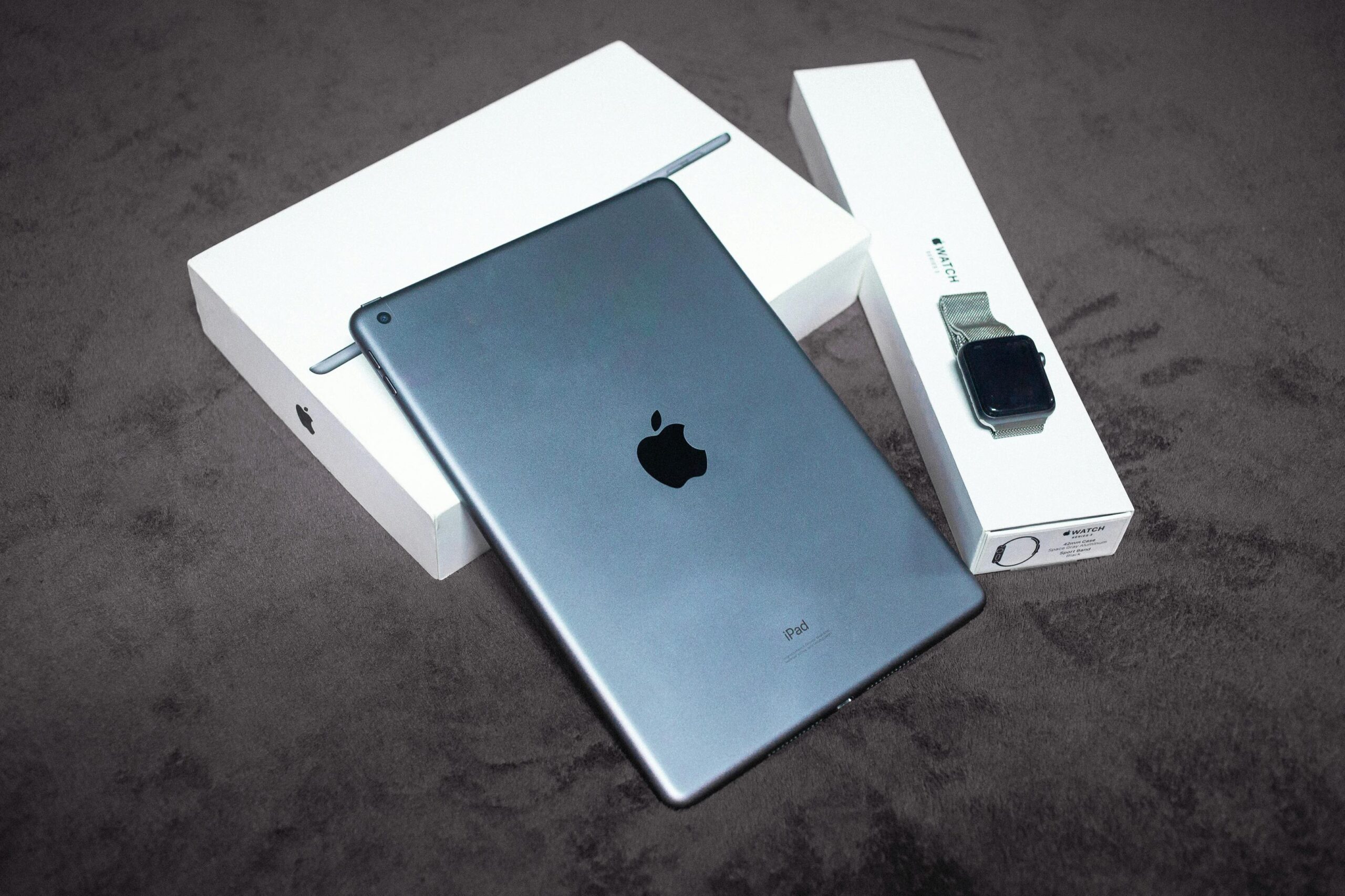 iPad and Apple Watch displayed on a black background, highlighting sleek design and packaging.